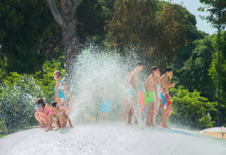 Children play in water spray on a large splash pad at Park Albatros Village, Tuscany, Italy in summer.