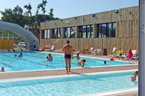 Buitenzwembad met bezoekers, ligstoelen en modern gebouw in hu Park Albatros Village, Toscane, Italië.