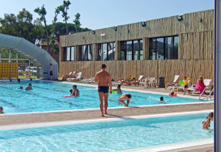 Outdoor swimming pool with guests, sun loungers and modern building at hu Park Albatros Village, Tuscany, Italy.
