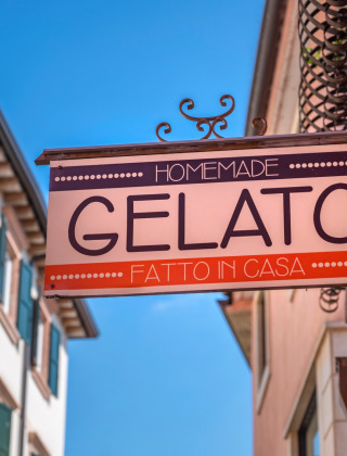 Cartel de gelato casero en San Vincenzo, Toscana, Italia, rodeado de edificios de colores pastel y cielo azul.