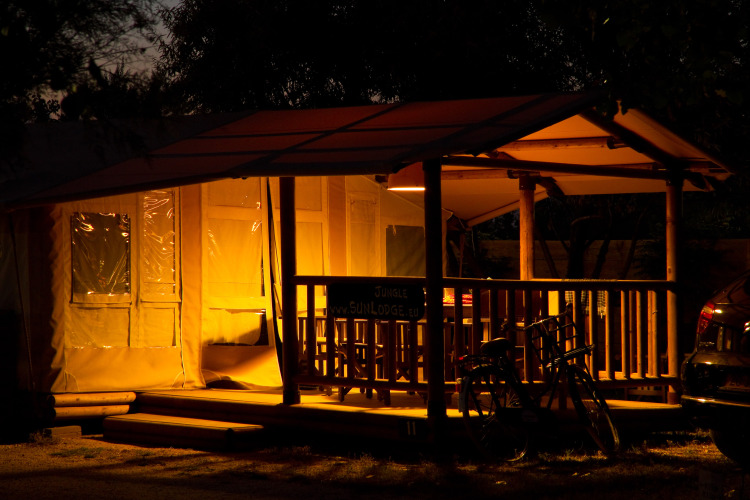 SunLodge Jungle iluminada con porche y bicicletas por la noche en Camping Village Cavallino, Italia.