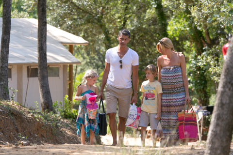 Familie går gennem skoven ved SunLodge Jungle på Camping Village Cavallino i Italien, bærer tasker og håndklæder.