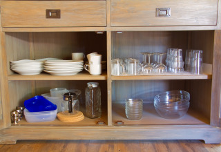 Open kast met servies, bekers, glazen en kommen in SunLodge Jungle te Camping Village Cavallino, Italië.