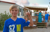 Niño sostiene llaves frente a SunLodge Redwood en Camping Village Cavallino, Italia, con su familia al fondo.