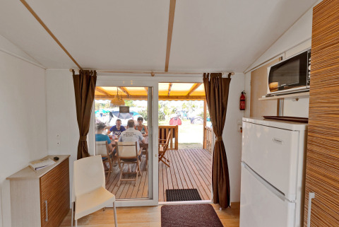 Binnenzicht van een SunLodge Redwood op Camping Village Cavallino in Italië, mensen zitten buiten aan tafel.