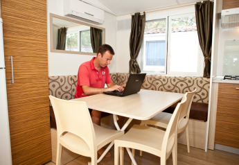 Man working on a laptop at a dining table in the SunLodge Redwood at Camping Village Cavallino, Italy.