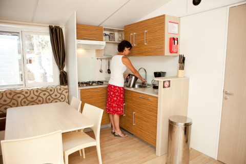 Vrouw kookt in moderne keuken in SunLodge Redwood op Camping Village Cavallino, Italië.
