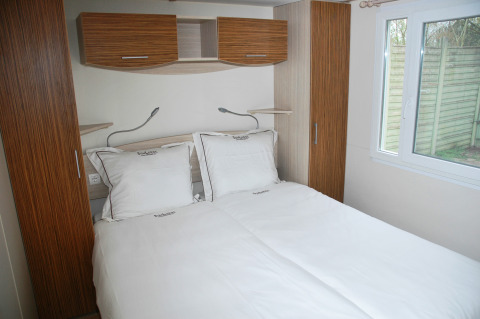 Slaapkamer met dubbel bed bij SunLodge Redwood in Camping Village Cavallino, Italië. Lichte meubels, raam.