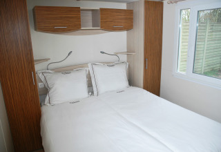 Slaapkamer met dubbel bed bij SunLodge Redwood in Camping Village Cavallino, Italië. Lichte meubels, raam.