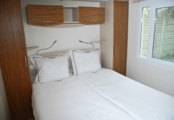 Bedroom with double bed at SunLodge Redwood, Camping Village Cavallino, Italy. Light wood furniture, window.