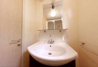 Moderne badeværelse med hvid håndvask, spejl og hylde i SunLodge Redwood på Camping Village Cavallino, Italien.