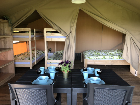 Interieur van een safaritent op Camping de Regenboog met eettafel, stapelbedden en een tweepersoonsbed.