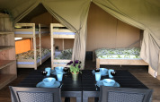 Vista interior de una tienda safari en Camping de Regenboog, con mesa de comedor, literas y cama doble.
