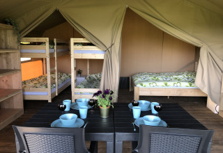 Vista interior de una tienda safari en Camping de Regenboog, con mesa de comedor, literas y cama doble.