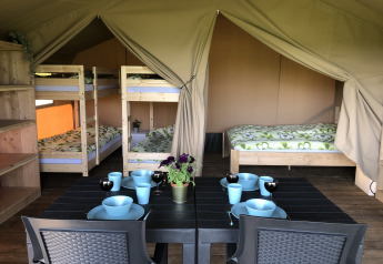 Vista interior de una tienda safari en Camping de Regenboog, con mesa de comedor, literas y cama doble.