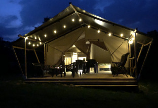 Tienda safari iluminada de noche en Camping de Regenboog, República Checa, con asientos en la terraza.