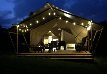 Tienda safari iluminada de noche en Camping de Regenboog, República Checa, con asientos en la terraza.