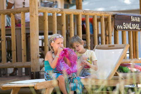 Dos niños juegan, uno infla un globo, frente a una cabaña en SunLodge Safari, Camping Village Cavallino, Italia.