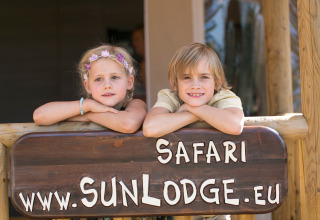 Twee kinderen leunen op een SunLodge Safari-bord in Camping Village Cavallino (Suncamp), Italië.