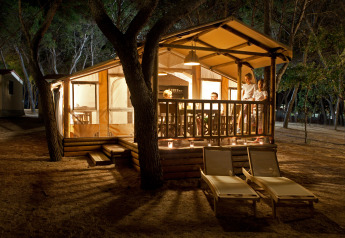 SunLodge Safari tent at Camping Village Cavallino in Italy, warmly lit at night with people relaxing on the porch.