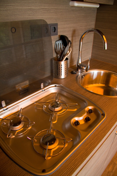 Moderne keuken met gasfornuis, spoelbak en keukengerei in SunLodge Safari op Camping Village Cavallino in Italië.