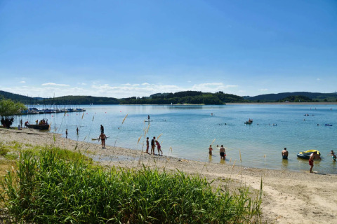 Huéspedes en un parque vacacional disfrutando de la playa y el lago bajo el sol en plena naturaleza.
