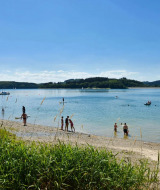Huéspedes en un parque vacacional disfrutando de la playa y el lago bajo el sol en plena naturaleza.
