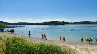 Huéspedes en un parque vacacional disfrutando de la playa y el lago bajo el sol en plena naturaleza.