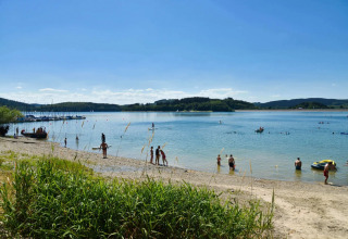 Vacation park guests swimming and relaxing by a clear lake and sandy beach on a sunny summer day.