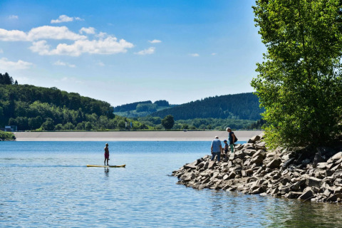 Parc de vacances au bord d’un lac avec des visiteurs profitant du glamping, d’activités nautiques et de la nature.
