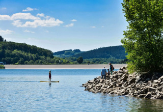 Parco vacanze sul lago con ospiti che praticano glamping, sport acquatici e ammirano verdi colline alberate.