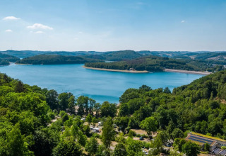 Udsigt over en smuk sø omgivet af frodige skove i et feriepark med glamping indkvarteringer.