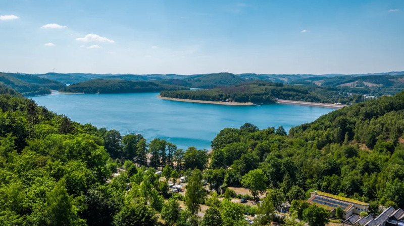 Blick auf einen See, umgeben von Wäldern, im Ferienpark mit Glamping-Unterkünften an sonnigem Tag.
