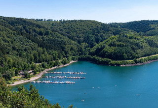 Vista de un lago rodeado de bosque, embarcadero y áreas de glamping en un parque vacacional.