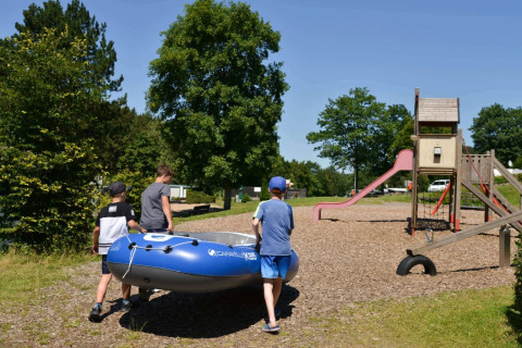 Bambini portano un gommone vicino a un parco giochi in un villaggio vacanze con sistemazioni glamping.
