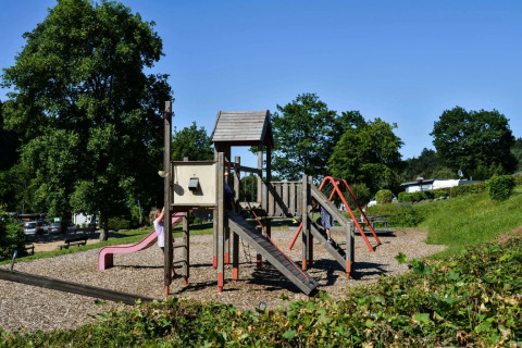 Spielplatz im Ferienpark mit Glamping, Kinder spielen auf der Rutsche und Klettergerüst im Grünen.