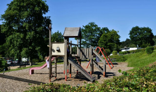 Parque infantil en un complejo de glamping, niños jugando en el tobogán y columpios rodeados de naturaleza.