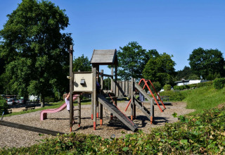 Speeltuin aan een vakantiepark met glamping, kinderen spelen op glijbaan en klimrek tussen het groen.