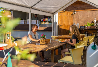 To personer nyder et måltid ved et udendørs spiseområde i en feriepark med glamping faciliteter.