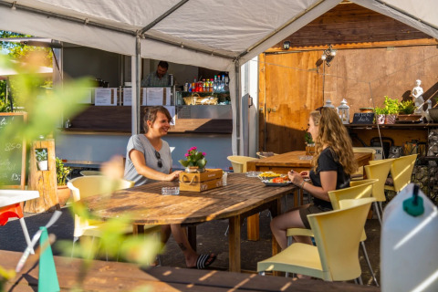 To personer nyder et måltid ved et udendørs spiseområde i en feriepark med glamping faciliteter.