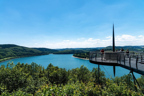 Uitkijkplatform over een meer en groene heuvels in een vakantiepark met glamping-accommodaties.