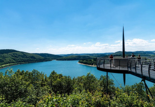 Viewing platform overlooking a lake and green hills in a holiday park with glamping tents and nature views.