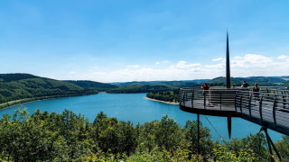 Plataforma panorámica con vistas al lago y colinas verdes en un parque vacacional con alojamiento glamping.