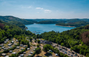 Parque vacacional con glamping junto a un lago pintoresco, rodeado de bosques y colinas, vista aérea.