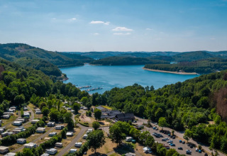 Ferienpark mit Glamping-Unterkünften am See, umgeben von Wäldern und Hügeln, aus der Luftansicht.