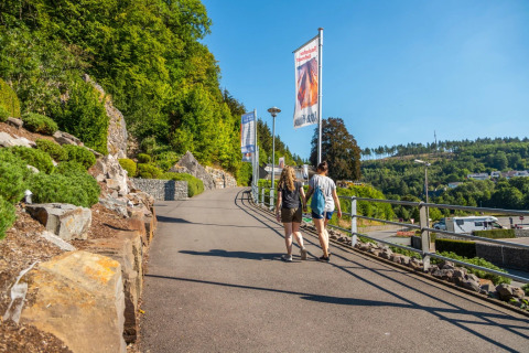 Deux personnes marchent sur un sentier d'un parc de vacances avec glamping, entourées de collines vertes.