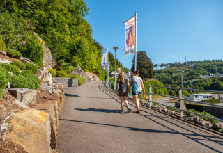 Deux personnes marchent sur un sentier d'un parc de vacances avec glamping, entourées de collines vertes.