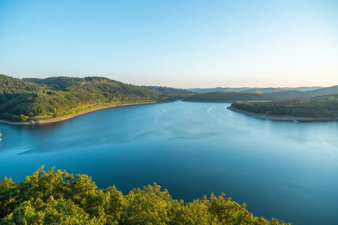 Vista de un lago tranquilo rodeado de colinas verdes, tomada desde un parque vacacional con glamping.