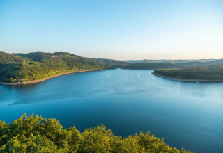 Vue sur un lac paisible entouré de collines boisées, prise depuis un parc de vacances avec glamping.