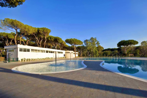Piscina e strutture moderne al Camping Village Roma Capitol in Toscana, Italia, immerso tra alberi di pino.